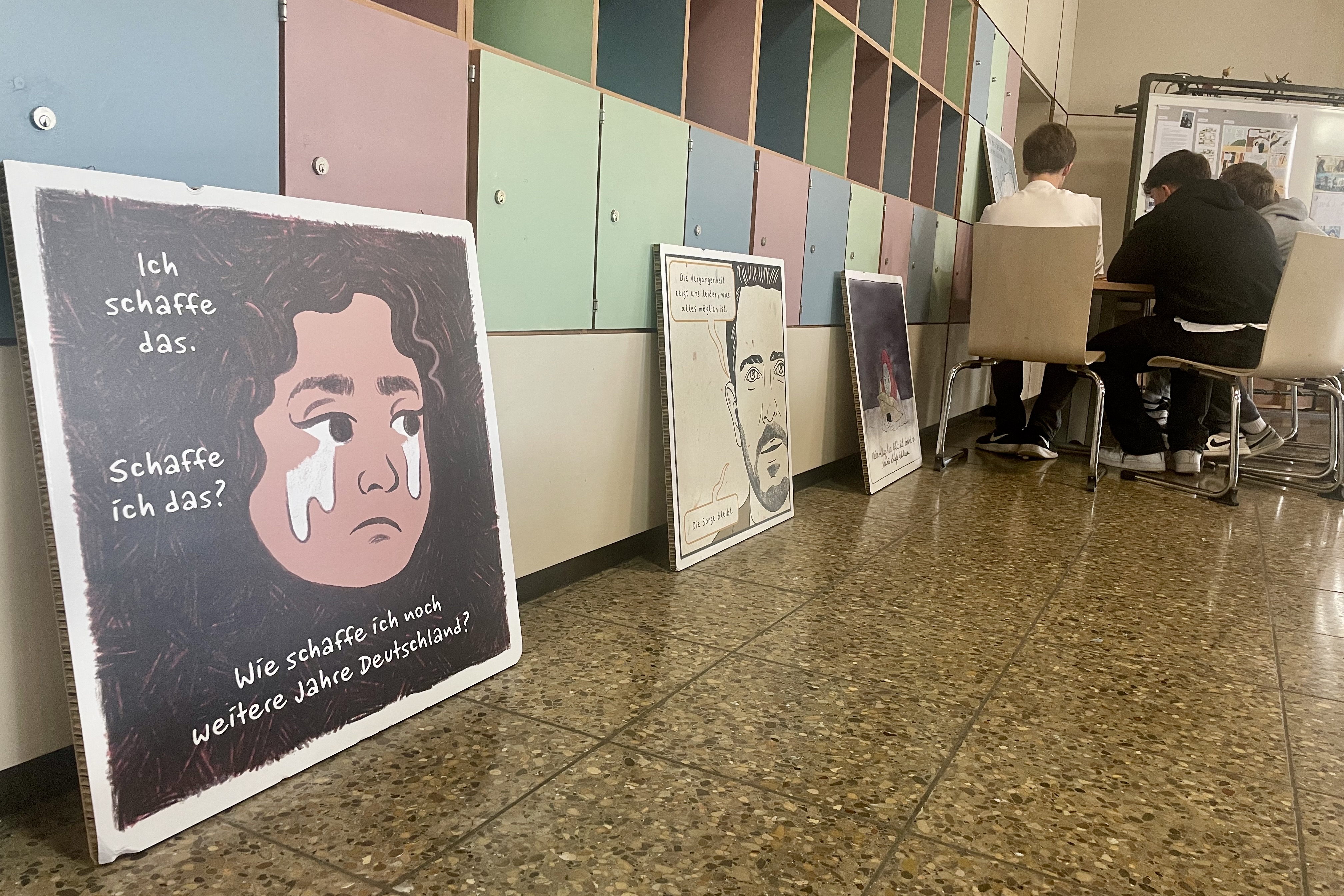 Drei Ausstellungstafeln mit Comics stehen auf dem Boden eines Klassenzimmers.