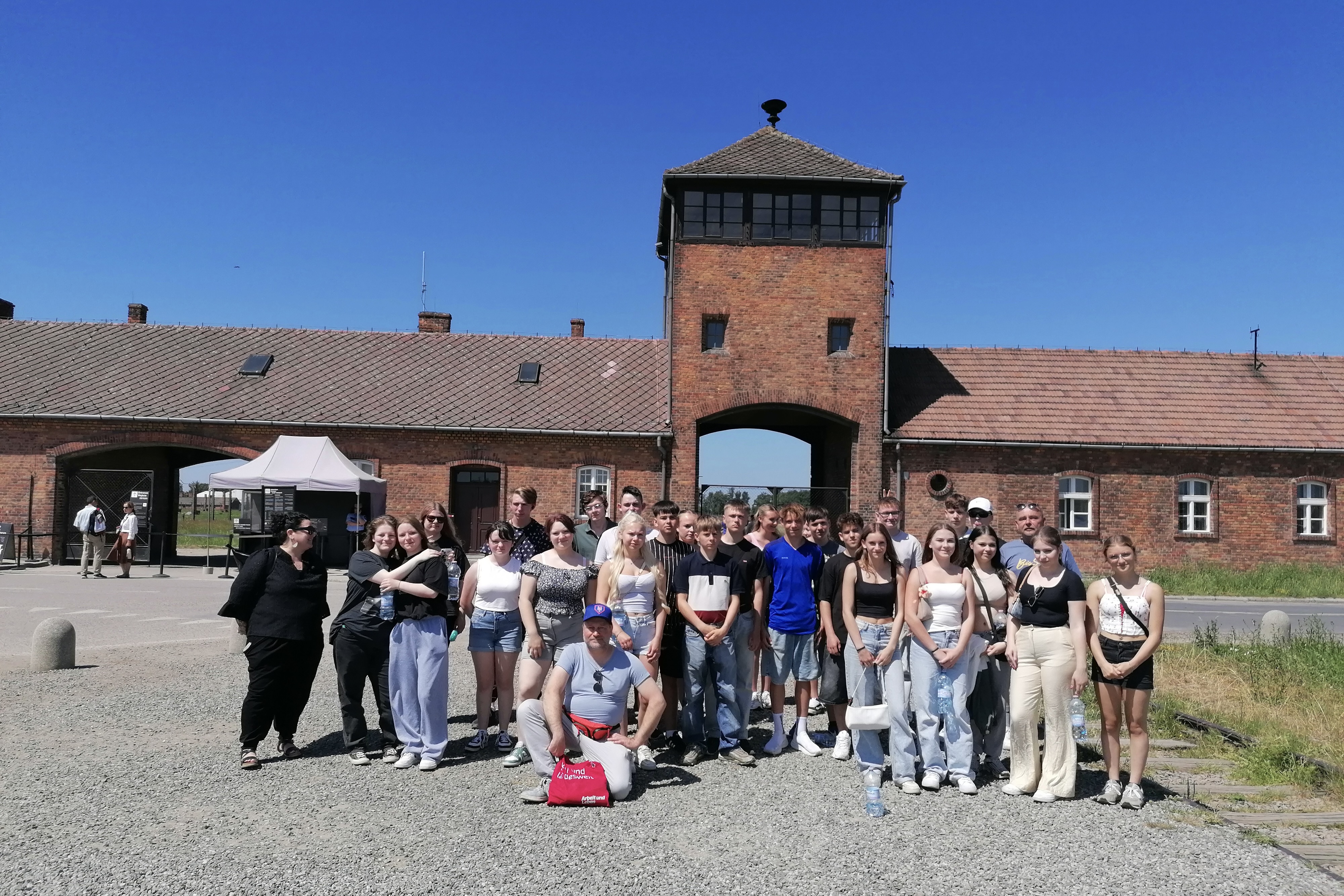Eine Gruppe steht vor dem Eingang der Gedenkstätte. Die Menschen schauen ernst und nach vorn in die Kamera.