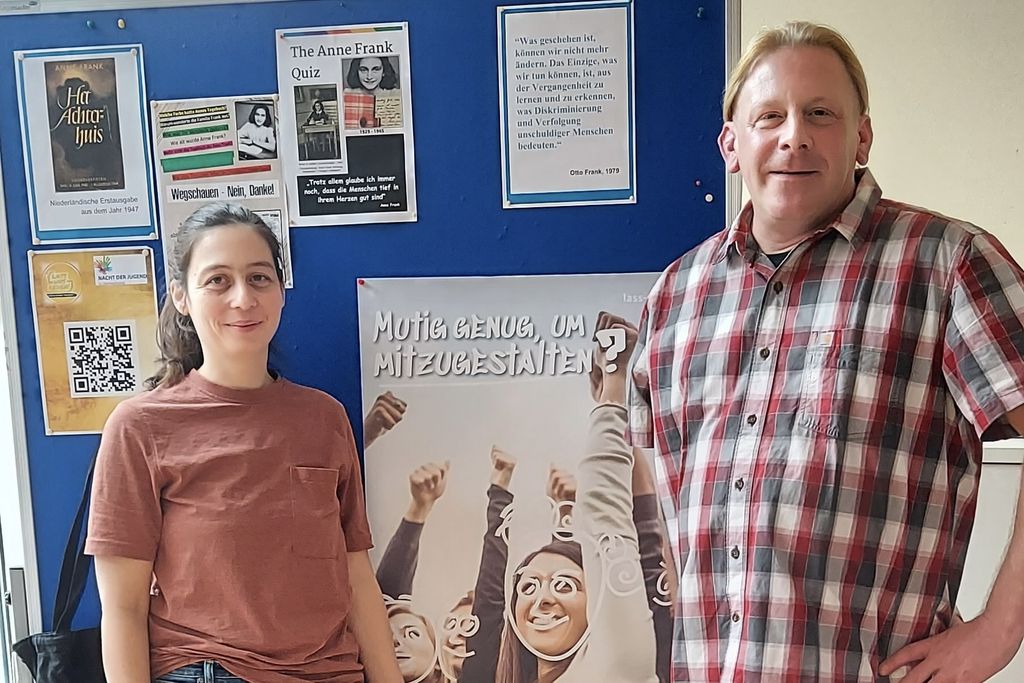 Julia Zylla, links im Bild, und Respekt Coach Oliver Hoyer, rechts im Bild, vom JMD Delmenhorst stehen vor einer blauen Pinnwand. An der Pinnwand hängen Blätter und unter anderem ein Poster zum Programm Respekt Coaches, auf dem steht "Mutig genug, um mitzugestalten?"